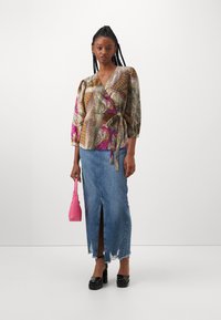 A patterned wrap top with three-quarter sleeves, paired with a high-slit denim skirt and black platform shoes. Holding a small pink handbag.