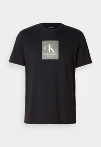 Camiseta negra de manga corta con un logo cuadrado gris que presenta un gran "cK" y el texto "Calvin Klein NEW YORK" centrado en el pecho.