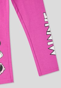 Różowe legginsy z graficznym wizerunkiem postaci z kreskówki i czarnymi akcentami. Materiał jest gładki, a na designie znajduje się słowo „MINNIE” w dużych białych literach.