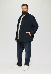 Granatowa kurtka wykonana z bawełny, z zapięciem na guziki i bocznymi kieszeniami, założona na jasny sweter, połączona z ciemnymi dżinsami i białymi sneakersami.