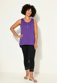 Top viola senza maniche in stile henley, con tasca frontale e jeans neri con orlo borchiato. Indossato con sandali argento.