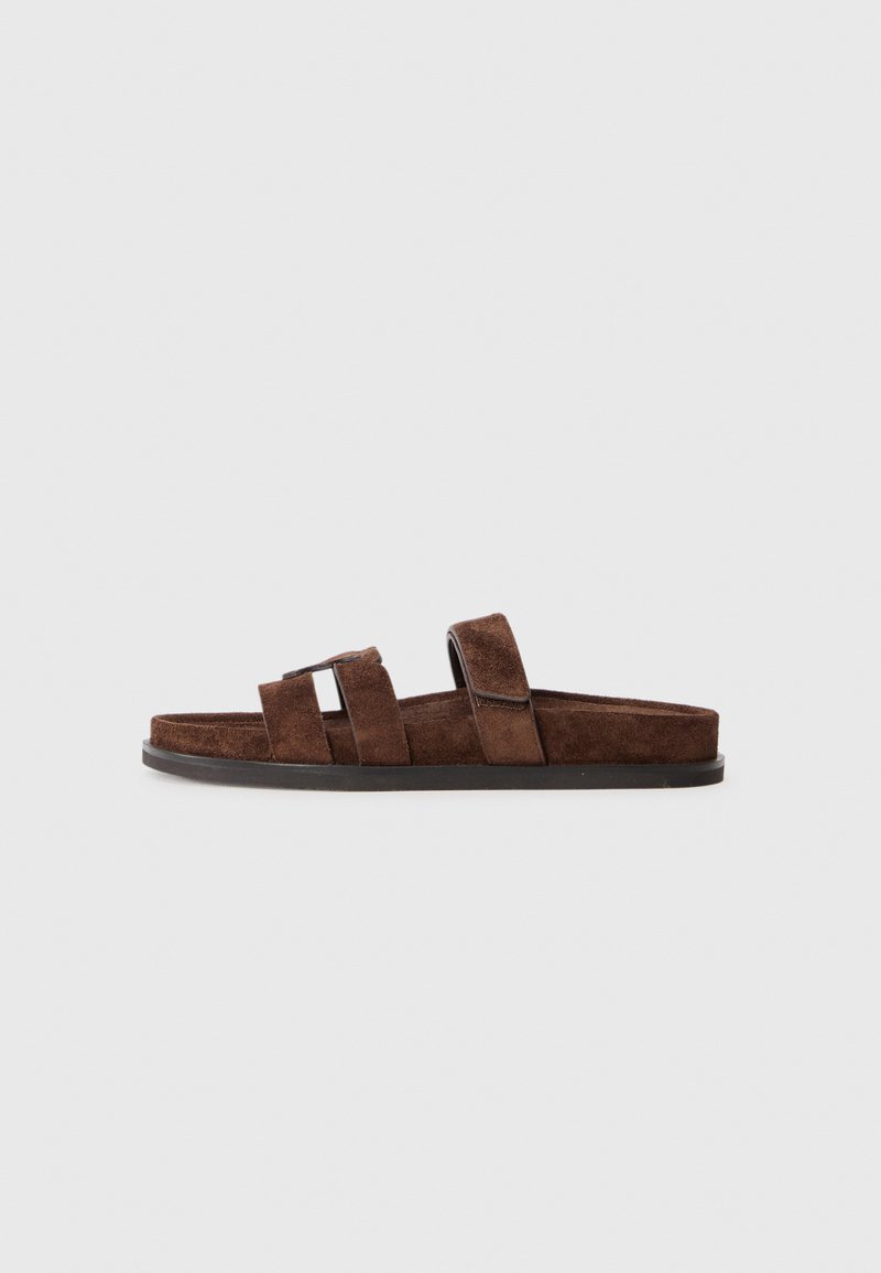 Brown suede slide sandal with three straps and a flat black sole on a white background.