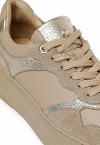 Beige lenkkarit metallinhohtoisilla kullansävyillä, mokkaa ja nahkaa, tuntumaltaan erilaisilla pinnoilla, pyöreillä nauhoilla ja teksturoidulla pohjalla.