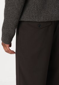 Grijze geribbelde trui met een brede ronde hals, gecombineerd met een bruine broek met een zijzak en knoopdetails. Gelaagd stof.