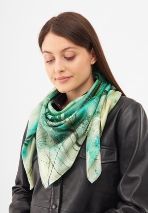 Écharpe en soie dans des nuances de turquoise et de vert, avec un motif de feuilles et une texture douce et fluide, stylée en forme triangulaire.