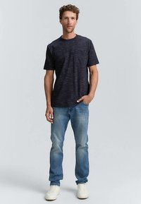 Tumši zila struktūrēta īsroku t-krekls ar krūšu kabatu, kombinēts ar gaiši zilām taisnām džinsa biksēm un baltiem sporta apaviem.