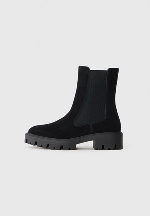 Bottines en daim noir à panneaux latéraux élastiques et semelle en caoutchouc épaisse. Caractéristiques d'une texture lisse et d'un design à bout rond.