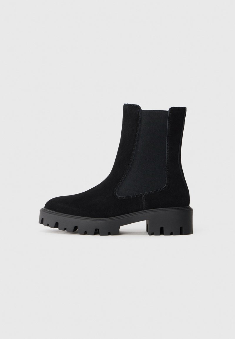 Svarte ankelboots i semsket skinn med elastiske sidepaneler og en chunky gummisåle. Har en glatt tekstur og design med rund tå.