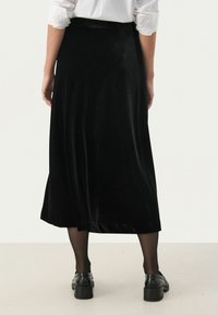 Schwarzer Samt-Midirock mit glatter Textur, A-Linie-Silhouette und einem leichten Glanz. Getragen mit schwarzen Schuhen und transparenten Strumpfhosen.