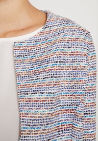Veste texturée multicolore présentant un motif tissé avec des rayures bleues, oranges et blanches. Design à col ouvert, matériau léger.