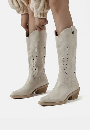 Stivali da cowboy in pelle grigia chiara con design ritagliati, punta affusolata e tacco a zeppa. Presentano accenti di cucitura e linguette per la calzata.