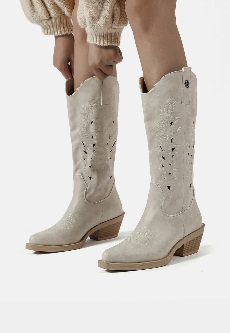 Stivali da cowboy in pelle grigia chiara con design ritagliati, punta affusolata e tacco a zeppa. Presentano accenti di cucitura e linguette per la calzata.