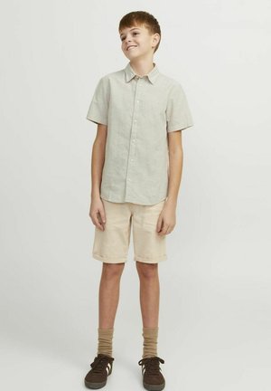 Camisa de manga corta gris claro hecha de una tela suave y texturizada; combinada con pantalones cortos beige con puños enrollados y zapatillas marrones con cordones negros.