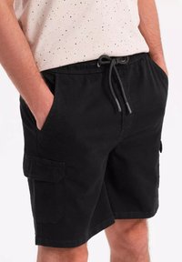 Shorts cargo noirs en coton avec taille à cordon, poches latérales et sur les jambes, et une coupe décontractée pour le confort.