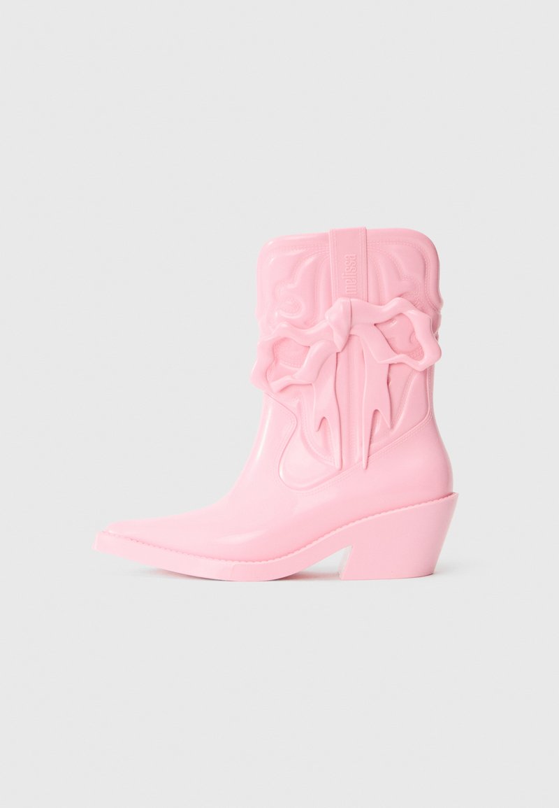 Botín de vaquero de plástico rosa con punta afilada y tacón grueso. Presenta un detalle de lazo elevado en el lateral y un logotipo embossado. Textura suave.
