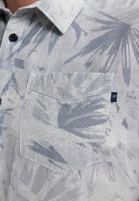 Camicia a maniche corte in tessuto leggero, con motivo a foglie blu, chiusura con bottoni e taschino sul petto con un piccolo tag del logo.