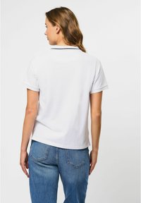 Witte polo met korte mouwen en een klassieke kraag, gecombineerd met blauwe high-waisted jeans. Gladde stof en een relaxte pasvorm.