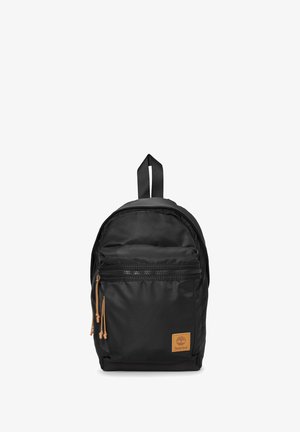 Mochila negra hecha de nylon con forma redondeada, que cuenta con un bolsillo delantero con cremallera, detalles en color marrón claro y un asa superior para llevarla.
