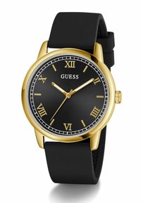 Black round watch with gold accents, Roman numerals, and a gold bezel, featuring a black rubber strap and a minimalist dial design.