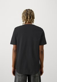 Sort kortærmet T-shirt med afrundet kant og en glat bomuldsstruktur, set fra ryggen, med minimalistisk design.