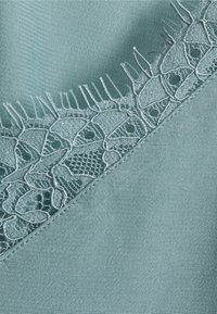 Mintgrønt stof med en glat tekstur har indviklet lyseblåt blonderkant langs en kant, der viser et åbent mønster.