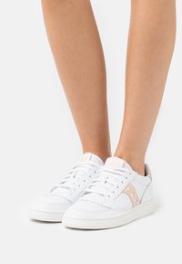 Sneakers bianchi con tomaia in pelle liscia, dettagli rosa, punta rotonda, suola piatta in gomma bianca e dettagli perforati sulla punta.