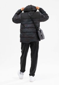 Czarna i ciemnoszara ocieplana kurtka z kapturem, z wzorem w kamuflaż i puchem. Nosi ją na czarnych spodniach i białych trampkach.
