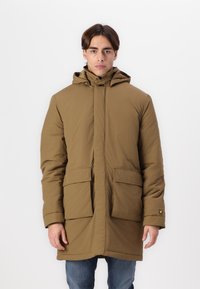Bruine gewatteerde parka met een professionele rits aan de voorkant, twee grote zakken en een textuurstof. Voorzien van warme isolatie en een logo op de mouw.