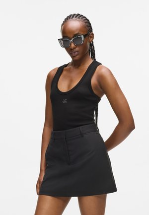 Débardeur noir côtelé avec des bretelles larges, associé à une mini jupe noire. La tenue est complétée par des lunettes de soleil noires brillantes.