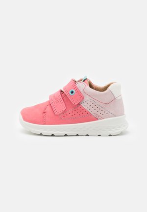 Chaussure en daim rose avec des accents blancs, dotée d'une bande velcro, d'un design perforé et d'une semelle en caoutchouc texturée, vue de côté.
