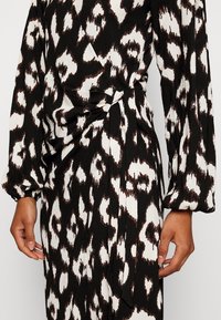 Svart och vit mönstrad klänning med en texturerad tyg. Har en omslagsdesign och puffärmar, smockad i midjan med insamlad detalj.