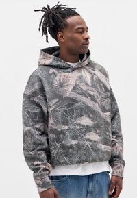 Hættetrøje med camouflage-design, der har grå, grønne og lyserøde bladmønstre. Blødt stof med løs pasform og foran lomme.