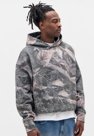 Sweat-shirt à capuche avec un design camouflage présentant des motifs de feuilles gris, vert et rose. Tissu doux avec une coupe décontractée et une poche avant.