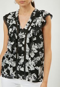 Schwarze Bluse mit floralen Mustern in Weiß, mit Rüschensleeves, V-Ausschnitt und Spitzenverzierungen entlang der Vorderseite und den Ärmeln.