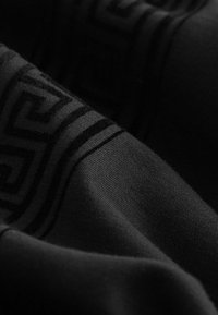 Černá tkanina s hladkým povrchem, která má jemný geometrický vzor v tmavším odstínu, vytvářející vrstvený, elegantní vzhled.