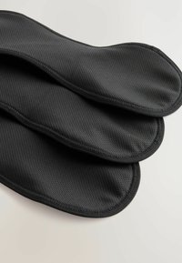 Sottopiedi imbottiti neri con una texture traspirante in rete, bordi arrotondati e cuciture visibili, sovrapposti leggermente a strati.