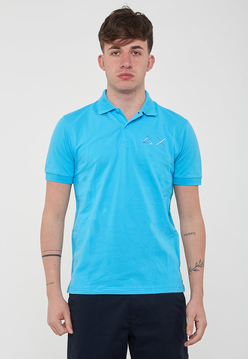 Polo shirt azzurro chiaro realizzato in tessuto morbido, con colletto, maniche corte e un piccolo logo ricamato sul lato sinistro del petto.