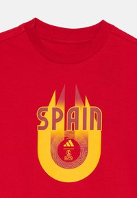 Rød bomull t-skjorte med rund hals. Midtstilt grafikk med "SPAIN" i gul og mørkgul med bølgemønstre og en rund logo.