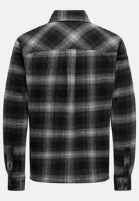 Camisa de franela a cuadros en blanco y negro, de mangas largas, con cuello, puños abotonados, tela texturada, que presenta un gran patrón de cuadros con elementos en contraste.