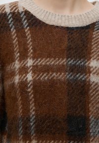 Gros plan d’un pull en laine à carreaux marron et beige avec un col rond côtelé beige.
