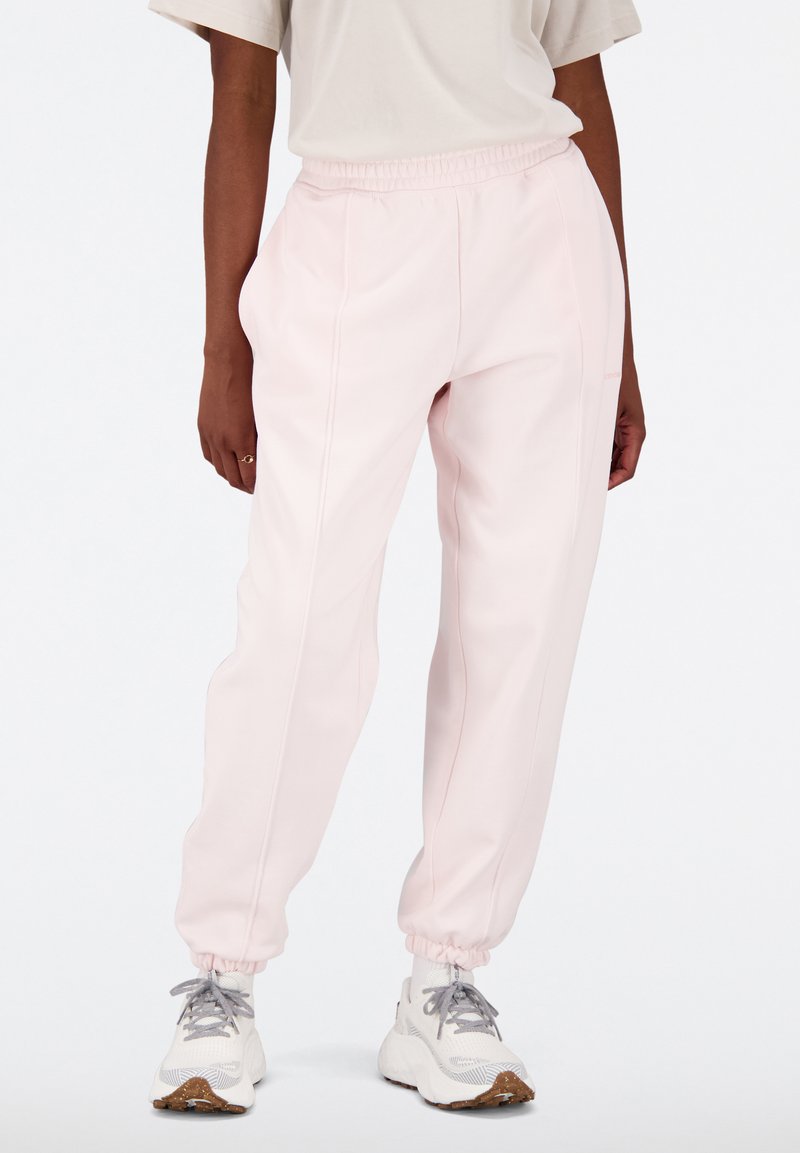 Pantalons de jogging rose clair avec taille élastique et chevilles élastiques. Fabriqués dans un tissu lisse avec des coutures latérales. Associés à des baskets blanches.
