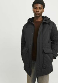 Schwarze Parkajacke mit Kapuze, einer vorderen Knopfleiste, zwei Brusttaschen und zwei Seitentaschen. Weicher Stoff mit lockerer Passform.