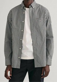 Zwart-wit geruit overhemd met een button-down kraag, lange mouwen en een borstzak, gedragen over een wit T-shirt.