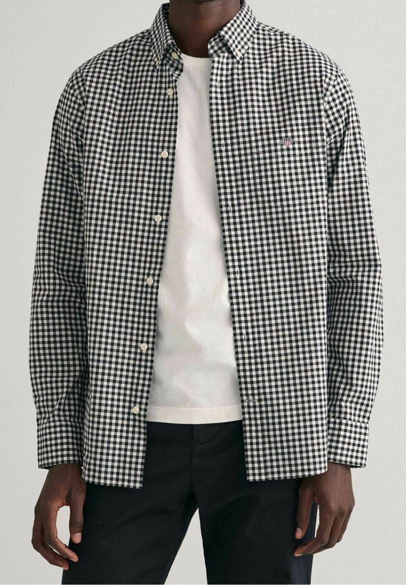 Zwart-wit geruit overhemd met een button-down kraag, lange mouwen en een borstzak, gedragen over een wit T-shirt.