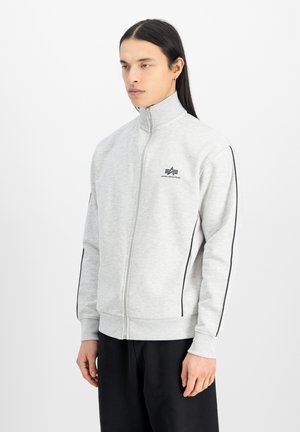 Grå zip-jakke med høj krave, sorte side striber og logo på brystet. Har ribbede manchetter og en glat, blød tekstur.