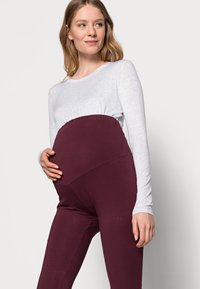 Maternity leggings in dark burgundy with a stretchy waistband, paired with a light grey long-sleeve top. Soft, comfortable cotton blend fabric.