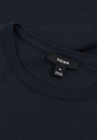 T-shirt nera con scollo rotondo con etichetta del marchio "REISS" visibile e taglia "M", prodotta in Vietnam.