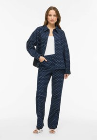 Granatowy komplet w groszki składający się z koszuli i spodni wykonanych z miękkiego materiału. Koszula ma kołnierzyk i przednie kieszenie; spodnie dopasowane, o kroju na miarę.