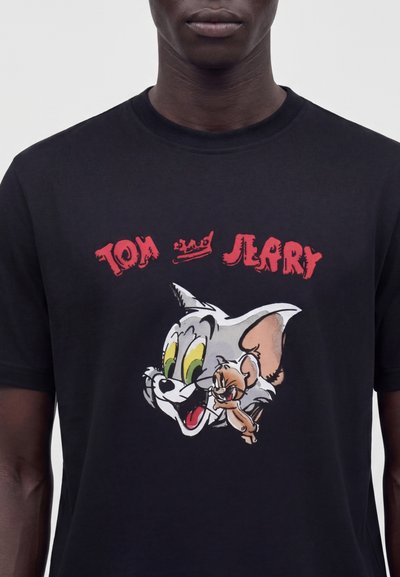 Μαύρο T-shirt με τους χαρακτήρες καρτούν Τομ η γάτα και Τζέρι το ποντίκι, με κόκκινο κείμενο "Tom Jerry" και μια μικρή κορώνα μεταξύ των ονομάτων.