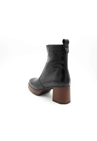 Bottine en cuir noir avec un bout rond, fermeture éclair sur le côté, et un talon de bloc de cinq centimètres avec une texture imitant le bois.